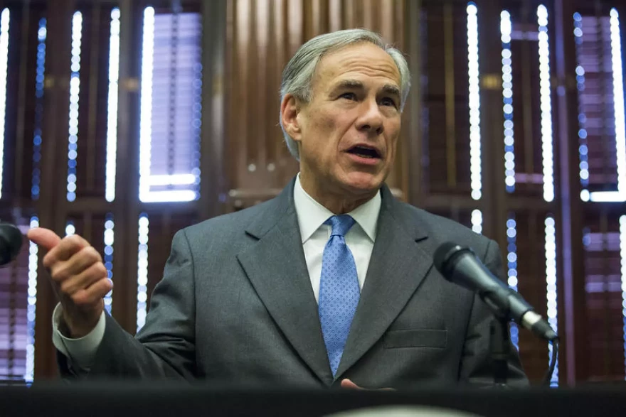 A photo of Texas Governor Greg Abbott at a podium speaking into microphones.