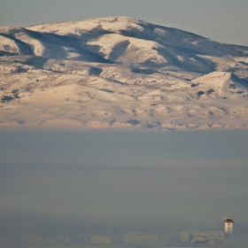 Snowy mountains with a thick inversion below them, nearly obscuring a small airport.