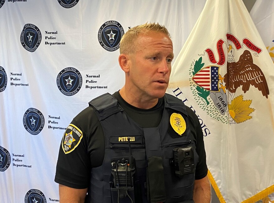 Police officer in security vest with two-way radio and body camera attached as he stands in front of a flag of Illinois