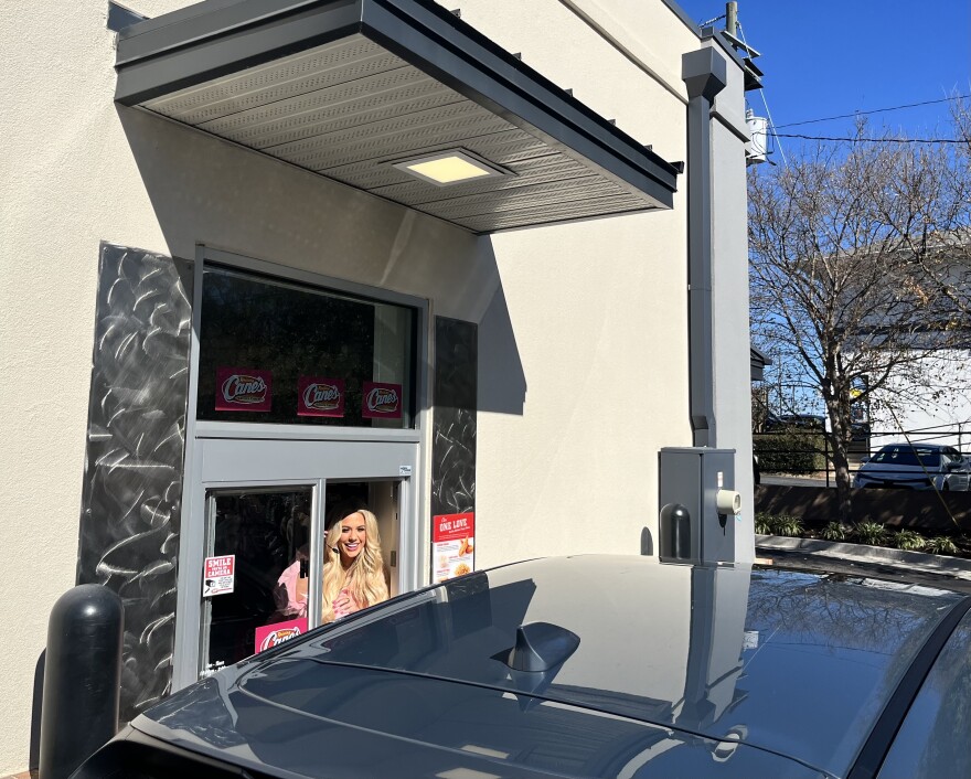 A lady smiling from inside a drive thru window into a car.