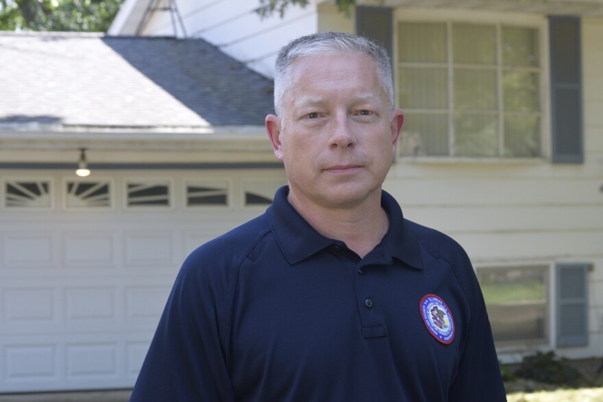 Man in a dark blue shirt and standing in front of a white house with an attached garage. 