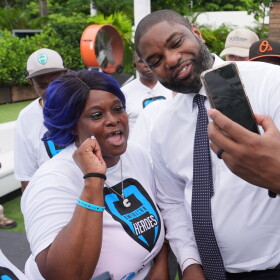 Black man in white dressshirt and tie  leans over to take a smartphone selfie with a shorter black woman in a white tshirt