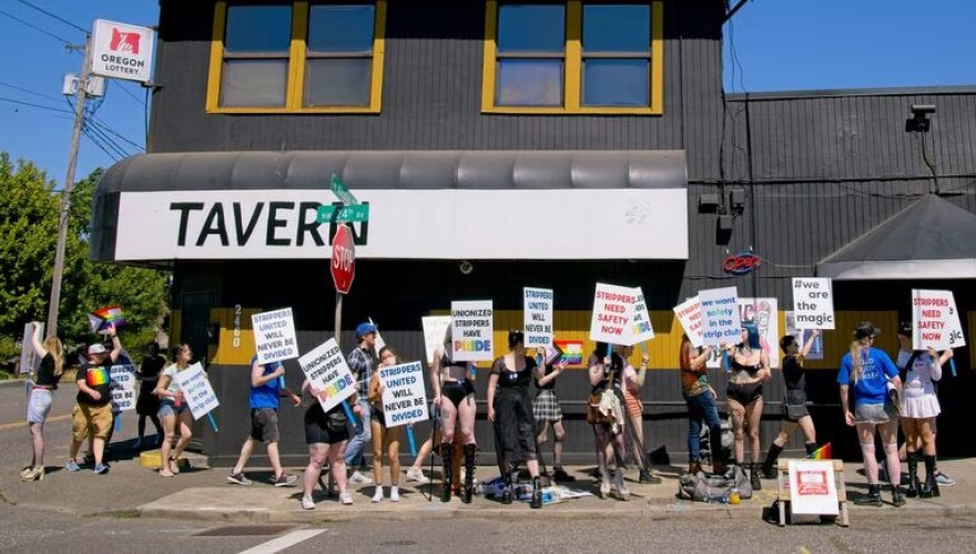 A line of people hold signs outside a building that reads "Tavern."