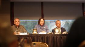 One woman sits at a table flanked by two older men