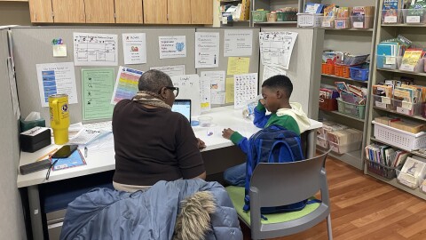 A child sits with his reading tutor at a desk in a room surrounded by bookshelves and reading posters at UW-Milwaukee.