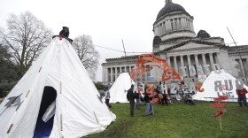 Environmental activists gather around structures erected on a grassy area in front of the Legislative building at the Capitol in Olympia, Wash., Monday, Jan. 8, 2018, the first day of the 2018 legislative session.