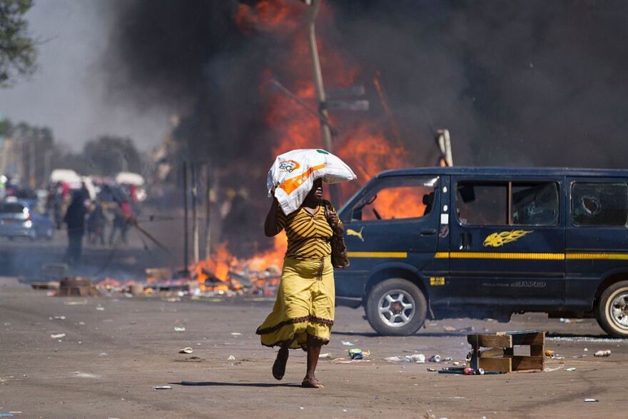 A woman carrying groceries on her head runs away as Zimbabwe's opposition supporters set up a burning barricade.