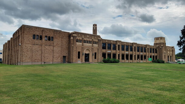 An elongated old brick school building on a slight grassy hill on an overcast day.