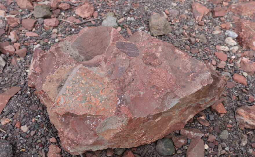A large red rock with various textures and colors sits on a bed of multicolored pebbles in the Keweenaw Peninsula
