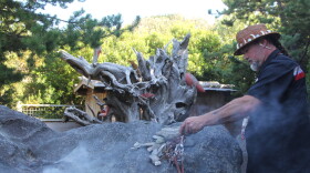 A man holds a burning piece of sage in a secluded garden memorial. 