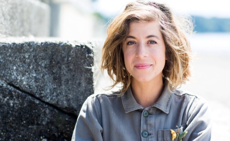 A woman wearing a blue button up shirt standing in front of a stone pillar.