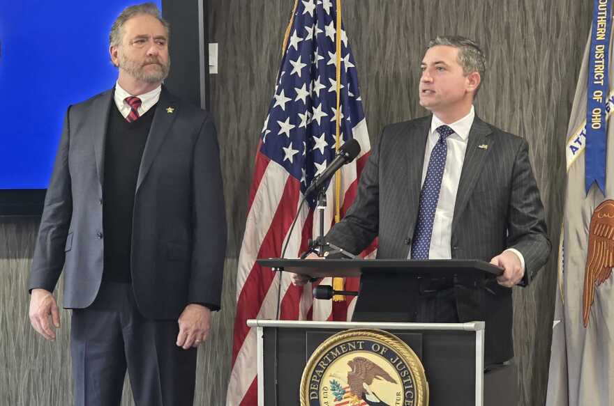 Two men stand at a podium with USA flag in background.