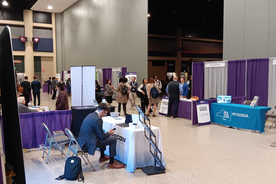 Attendees of the New York State Innovation Summit mingle in the section within the Buffalo Convention Center where booths were hosted by businesses and the state agencies that can help them with resources. Beyond the walls in the darkened section, a panel discussion was in progress.