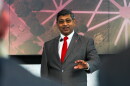 A man in a suit and tie with an OSU pin speaks on a stage. 