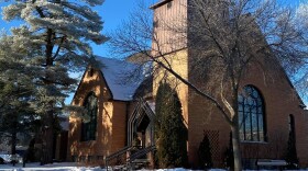 A stately brick church building in the winter with frost on surrounding pine trees against a bright blue sky.