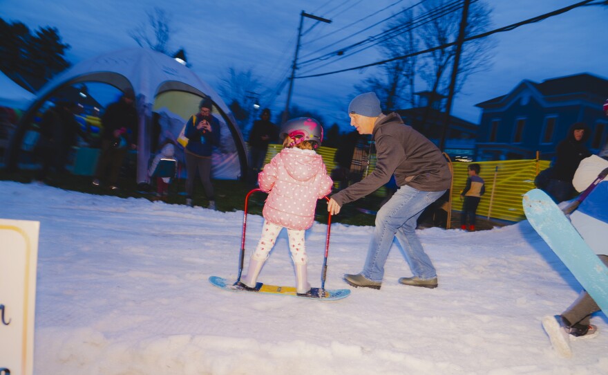 A man holds on to the support bar of a snowboard being ridden by a small girl.
