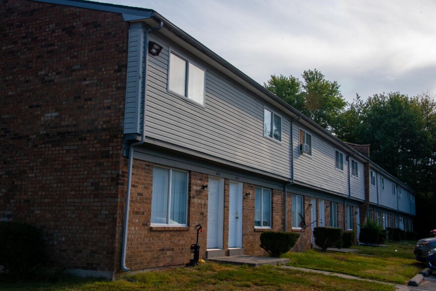 An apartment building in Poplar Hills brick first floor, vinyl siding top with trees and sky in background.