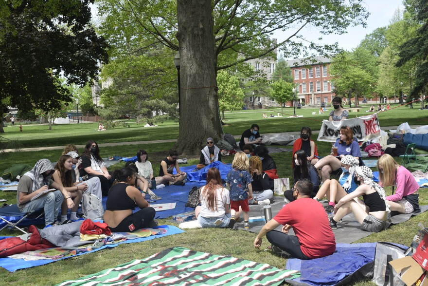 Students sit on blankets in a tree-shaded area gathered around in a circle