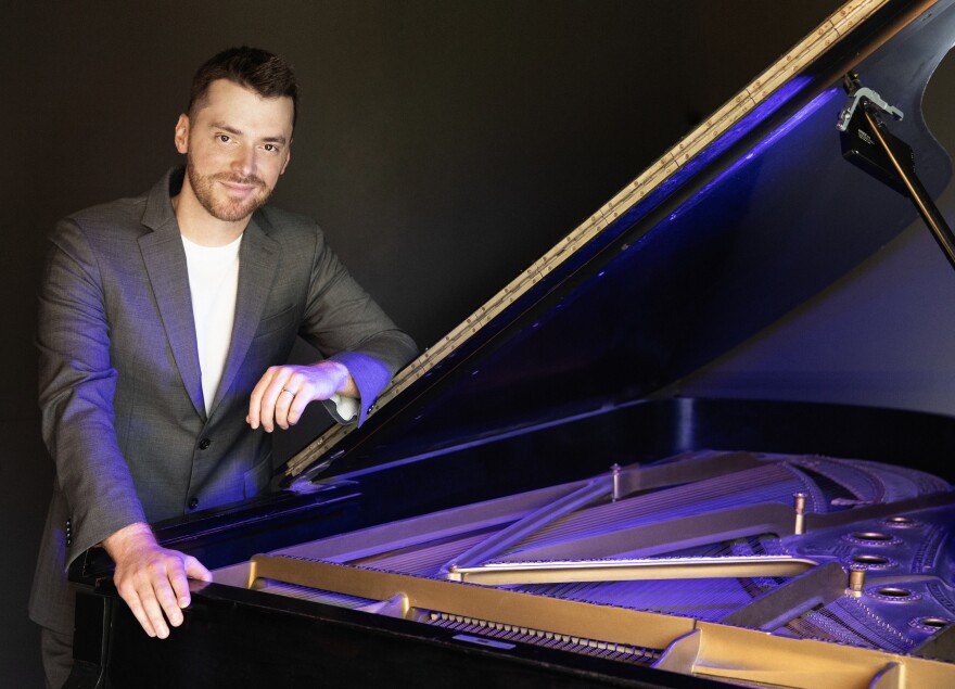 Peter Dugan stands leaning against an open piano