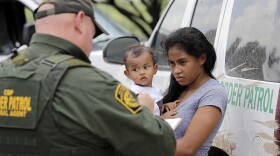 A mother migrating from Honduras holds her 1-year-old child as surrendering to U.S. Border Patrol agents after illegally crossing the border Monday, June 25, 2018, near McAllen, Texas.