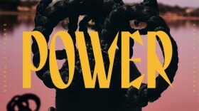 The back of a woman's head. Her hair is in intricate braids and she is wearing hoop earrings. The word "POWER" is over the photo in yellow text. 