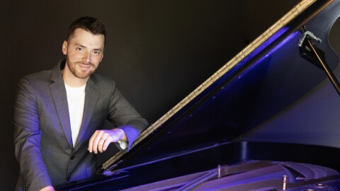 Peter Dugan stands leaning against an open piano
