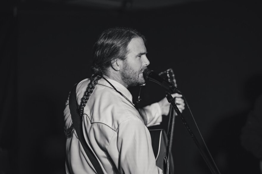 A man performing with an acoustic guitar and singing into a microphone.