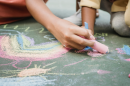 Close-up of two people drawing colorful chalk art on the pavement.