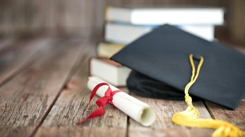 Diploma, graduation cap and books on wood table