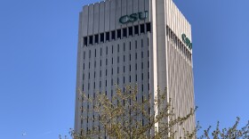 Green letters CSU on a high rise building over a tree.