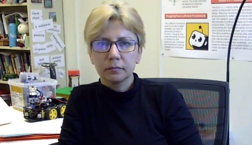 Woman in a black sweater and seated at a desk in an office with a bookshelf over her right shoulder and a toy tractor on her desk