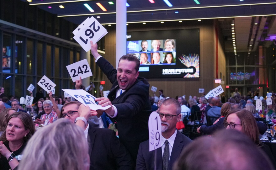 Auction cards are passed out at the 2026 Hear the Future gala. The man passing them out beams with excitement and makes a wild gesture.