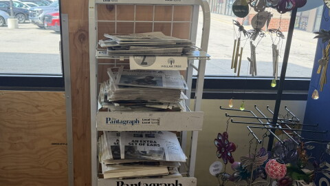 An in-store newsstand with stacks of newspapers placed inside of a window.