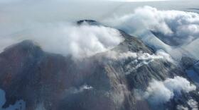 A volcanic dome and crater surrounded by clouds and fog