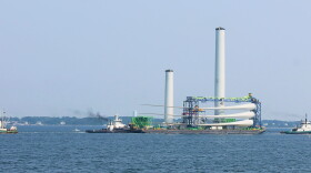 A barge departs from New Bedford Harbor carrying the major components for the first offshore wind turbine for Vineyard Wind: three tower sections (two of which are already connected), three blades, and a nacelle, Sept. 6, 2023.