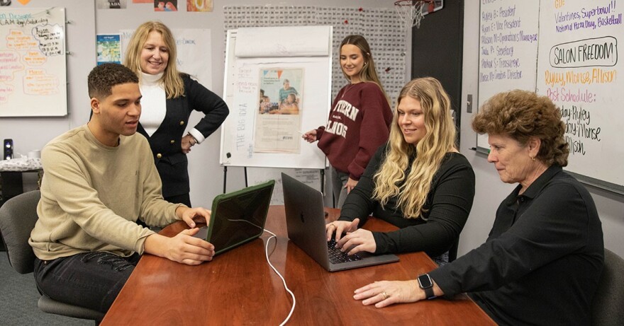 Students and a faculty advisor it at a table to work on a digital project together.