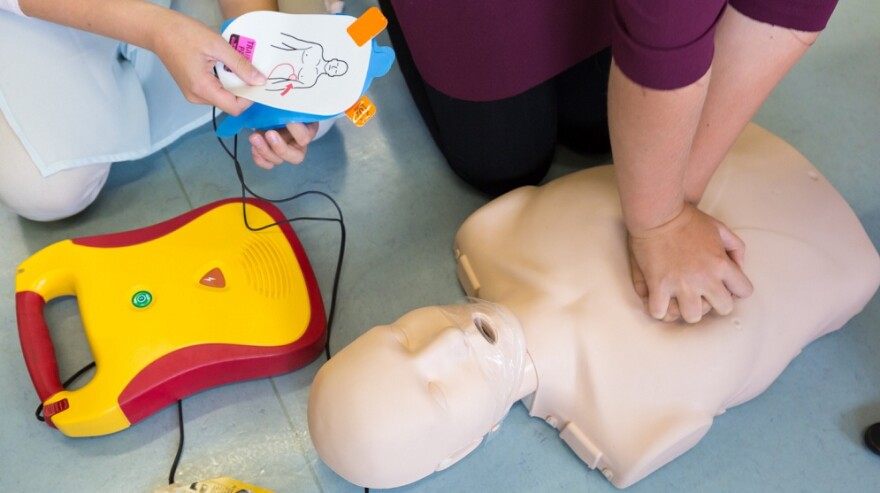 A CPR instructor demonstrates chest compressions on a training dummy as an AED is prepared for use, illustrating life-saving techniques for sudden cardiac emergencies.