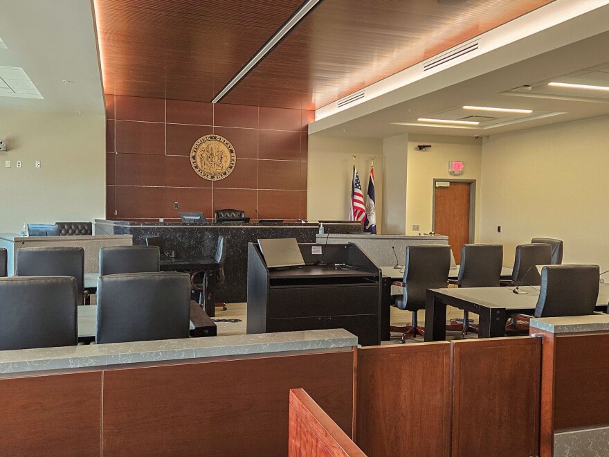 An empty courtroom with chairs and tables in front of a judge’s bench.