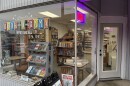 Looking into the windows of a small bookstore called Steve's Book-O-Rama. The name of the store is on the plate glass with old fashioned futuristic lettering, reminiscent of The Jetsons, with "we buy and sell" in a sans serif font underneath.