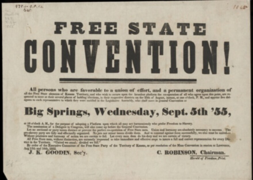 A black and white photograph depicting three women working on an assembly line, seated behind metal bars, and packaging small, dark items into wooden crates.