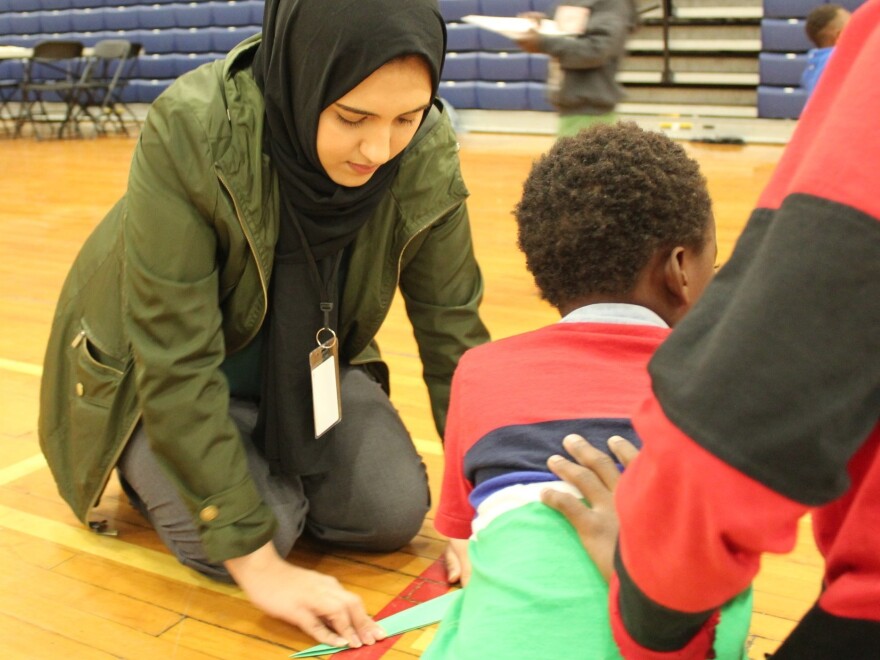 A volunteer folds paper airplanes with a young boy inside the Expo Building in Portland, Maine. Hundreds of migrants, many from Africa, have arrived there this month, and the city has converted the building into an emergency shelter to house them.