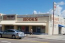 A light brown building that says Haslam's Book Store at the top and Books in large red lettering is seen from across a street with a man walking in front of it and a gray car passing to the left