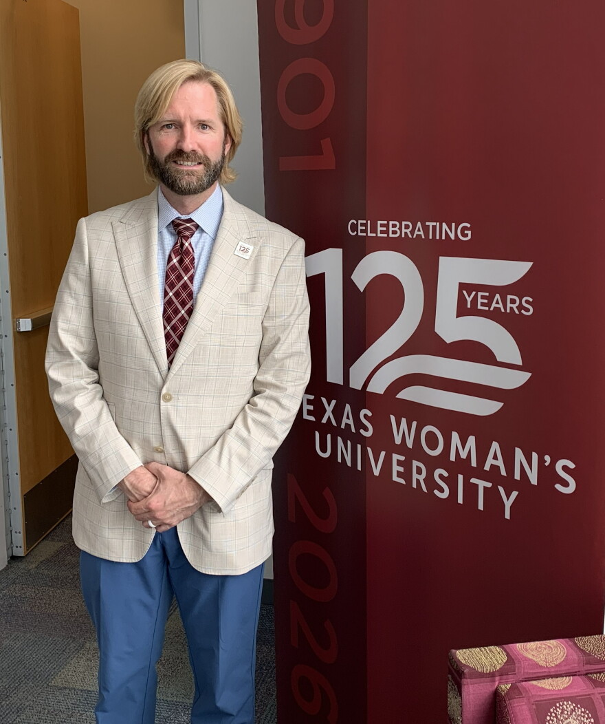 Blond haired, bearded man standing in front of TWU 125 years anniversary sign