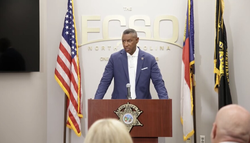 Sheriff Bobby Kimbrough behind a podium speaking at a press conference with three flags behind him. 