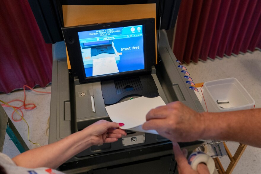 A polling judge helps guide a voter's ballot into a voting machine during the May 2022 Pennsylvania primary election.