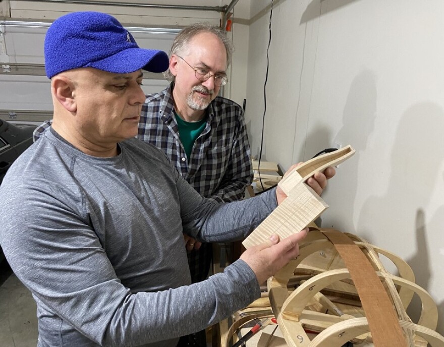 Luthiers George Wakim and Art Mize in Wakim's workshop. They are looking at pieces of wood that will be used to make a musical instrument.