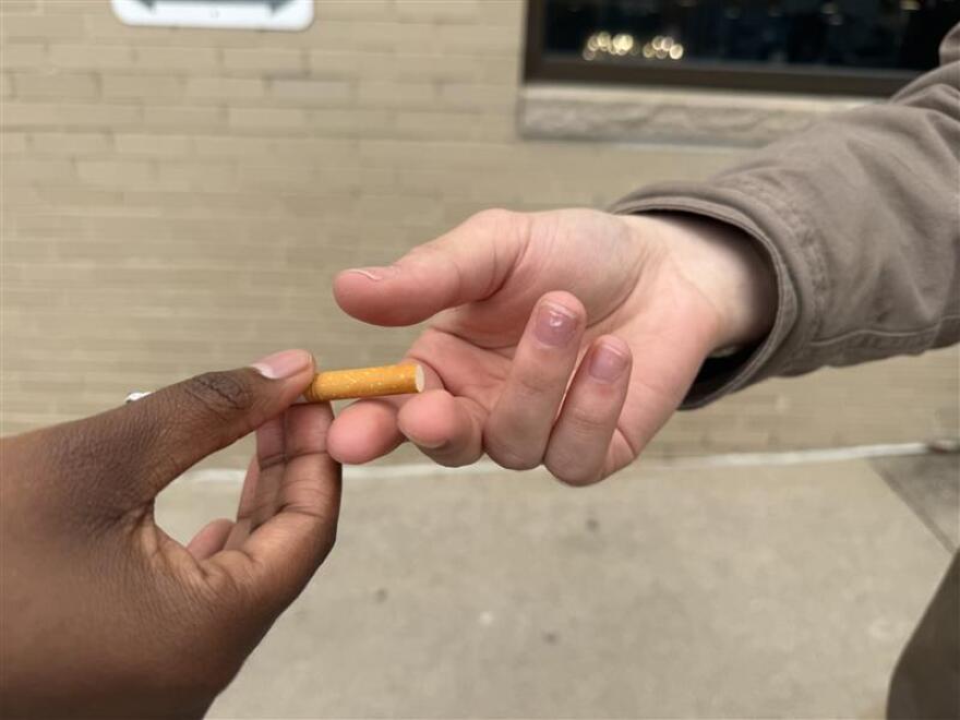 A closeup photo of two hands, one passing a cigarette to the other.