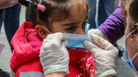 A woman places a protective face mask on a child as refugees and migrants wait to be transferred from the island of Lesbos to the Greek mainland. Public health officials worldwide have warned about the dangers of overcrowded refugee camps amid the COVID-19 pandemic. 