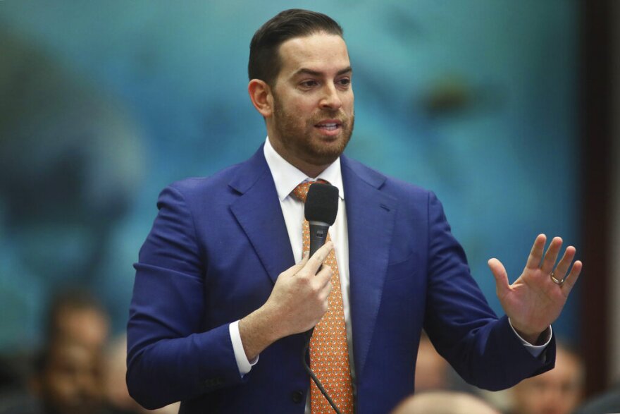 Man in suit holds a microphone and talks to a group 