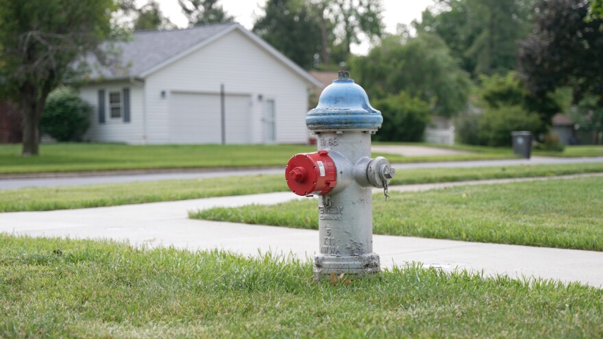 A grey fire hydrant with a bright red cap on the main outlet on a grassy area near a sidewalk. 